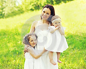Portrait happy smiling mother with two daughters children on the grass in a summer park
