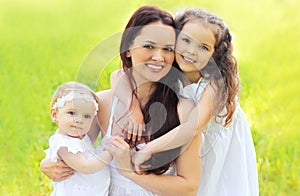 Portrait happy smiling mother with two daughters children on the grass in a summer park