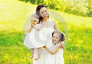 Portrait of happy smiling mother with two daughters children on the grass in summer park