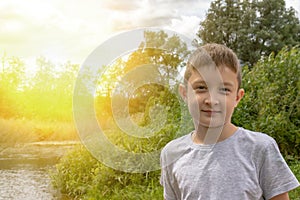 Portrait of happy smiling preteen boy outdoors in summertime, green nature and sunlight on background