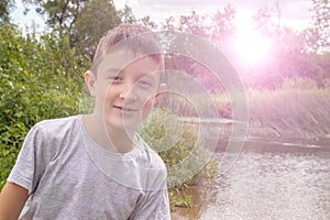 Portrait of happy smiling preteen boy outdoors in summertime, green nature and sunlight on background