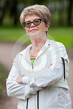 Portrait of happy smiling senior woman in sports suit standing with crossed hands