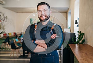 Portrait of happy smiling small business owner dressed in a black chef uniform with an apron in his cozy restaurant hall.