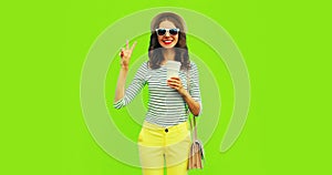 Portrait of happy smiling stylish young woman with coffee cup wearing handbag, striped t-shirt and summer straw round hat on green