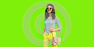 Portrait of happy smiling stylish young woman posing wearing handbag, striped t-shirt and summer straw round hat on green