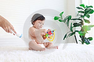 Portrait of happy smiling toddle baby girl sit on fluffy white rug with mother hand hold dusting powder bottle, mom apply talcum