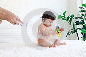 Portrait of happy smiling toddle baby girl sit on fluffy white rug with mother hand hold dusting powder bottle, mom apply talcum