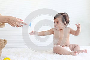 Portrait of happy smiling toddle baby girl sit on fluffy white rug with mother hand hold dusting powder bottle, mom apply talcum