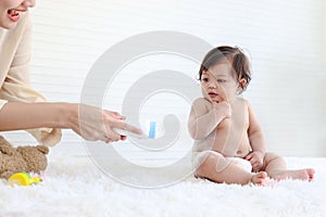 Portrait of happy smiling toddle baby girl sit on fluffy white rug with mother hand hold dusting powder bottle, mom apply talcum