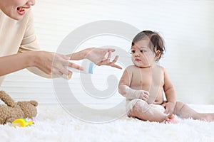 Portrait of happy smiling toddle baby girl sit on fluffy white rug with mother hand hold dusting powder bottle, mom apply talcum