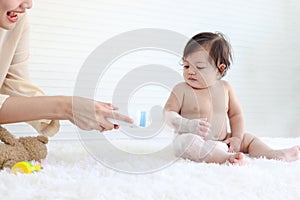 Portrait of happy smiling toddle baby girl sit on fluffy white rug with mother hand hold dusting powder bottle, mom apply talcum