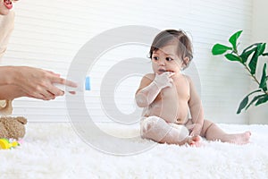 Portrait of happy smiling toddle baby girl sit on fluffy white rug with mother hand hold dusting powder bottle, mom apply talcum