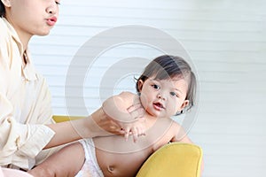 Portrait of happy smiling toddle baby lying on yellow sofa in living room at home, mother bonding with little girl daughter, mom photo