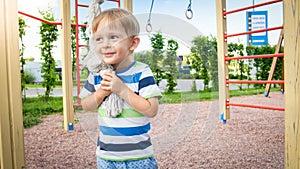 Portrait of happy smiling toddler boy playing with big rope for climbing on the children palyground at park. Active and photo