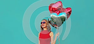 Portrait happy smiling woman with bunch of red heart shaped balloons on a blue background
