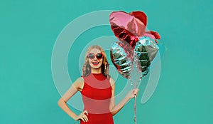 Portrait happy smiling woman with bunch of red heart shaped balloons on a blue background
