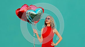 Portrait happy smiling woman with bunch of red heart shaped balloons on a blue background