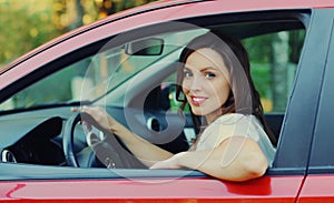 Portrait of happy smiling woman driver behind wheel red car