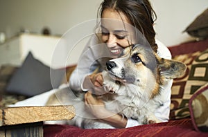 Portrait of happy smiling woman with her cute Welsh Corgi dog lying on couch at home.