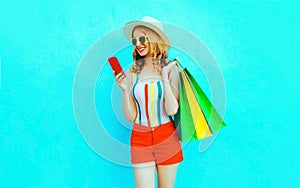 Portrait happy smiling woman holding phone with shopping bags in colorful t-shirt, summer straw hat, sunglasses, red shorts