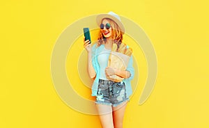 Portrait happy smiling woman holding smartphone, paper bag with long white bread baguette, wearing straw hat, shorts on colorful