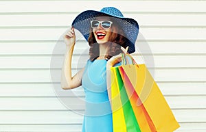 Portrait happy smiling woman with shopping bags wearing blue dress, summer straw round hat and sunglasses over white wall