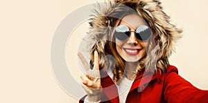 Portrait of happy smiling woman stretching hand for taking selfie with smartphone wearing jacket with fur hood