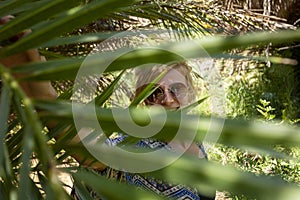 Portrait of happy smiling woman with sunglasses by branches of palm trees at tropical coast in Preveli beach on Crete island