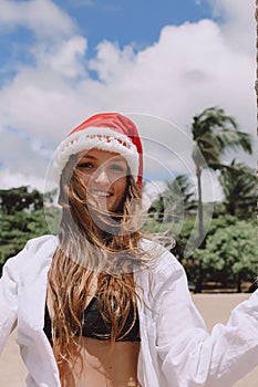 Portrait of happy smiling woman with tropical background at beach. Rear view of female is wearing Santa hat and bikini