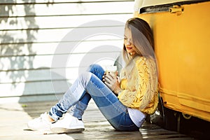 Pretty smiling woman is wearing yellow sweater drinking coffee latte near old retro bus