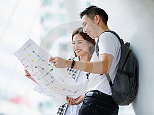 Portrait of happy smiling young adult Asian couple tourists standing and looking paper map together find a guide to a destination
