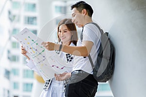 Portrait of happy smiling young adult Asian couple tourists standing and looking paper map together find a guide to a destination