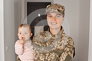 Portrait of happy smiling young adult woman soldier wearing camouflage uniform, returning home and being glad to meet her family,