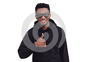 Portrait of happy smiling young african man showing thumbs up wearing a black hoodie, sunglasses isolated on a white