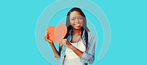 Portrait of happy smiling young african woman holding paper red heart on colorful blue background