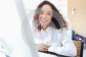 Portrait of happy smiling young beautiful woman with curly hair using desktop computer, female officer staff in casual white shirt
