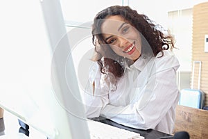 Portrait of happy smiling young beautiful woman with curly hair using desktop computer, female officer staff in casual white shirt