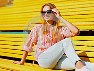 Portrait happy smiling young blonde woman sitting on bench in a city park