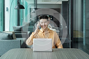 Portrait of happy smiling young business Asian, Chinese man person using laptop computer, working, and talking on smart mobile