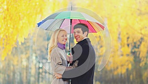 Portrait happy smiling young couple with colorful umbrella in warm sunny day on yellow leaves background