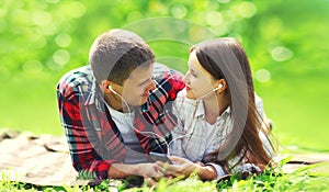 Portrait of happy smiling young couple listening to music in earphones with smartphone lying on the grass together in summer park