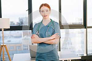 Portrait of happy smiling young female doctor wearing blue green uniform and stethoscope looking at camera.