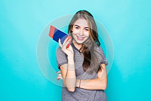 Portrait of a happy smiling young girl holding passport and travelling tickets isolated over blue background