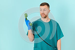 Portrait of happy smiling young male doctor with phone, on blue background.