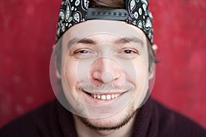 Portrait of happy smiling young man in a baseball cap and sweater on a red background