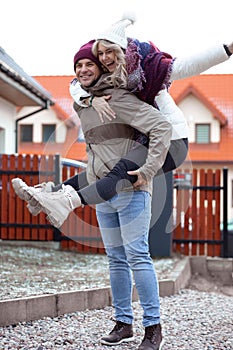 Portrait of happy smiling young man giving piggyback ride to beautiful woman in casual upper garments in yard. Family.