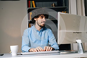 Portrait of happy smiling young man using computer and typing online message on wireless keyboard .