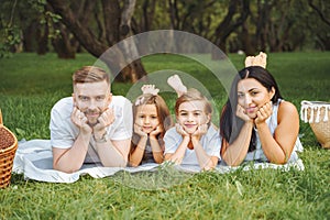 Portrait of happy smiling young parents and two children lying together on a picnic blanket at sunny day.