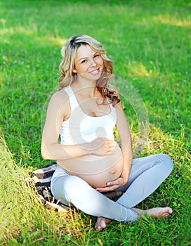 Portrait happy smiling young pregnant woman sitting on grass doing yoga