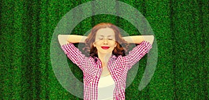 Portrait of happy smiling young relaxing woman lying on the grass background in park